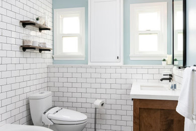 Design ideas for a small traditional bathroom in Los Angeles with shaker cabinets, medium wood cabinets, a corner bath, a shower/bath combination, white tiles, metro tiles, blue walls, porcelain flooring, a submerged sink, engineered stone worktops, blue floors, a shower curtain, white worktops, a single sink, a built in vanity unit and a one-piece toilet.