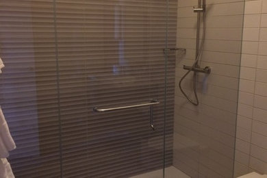 Example of a large minimalist master beige tile and ceramic tile corner shower design in Calgary with glass-front cabinets, beige walls and a hinged shower door