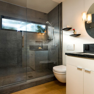 Aménagement d'une petit salle de bain rétro avec un placard à porte plane, des portes de placard blanches, un WC suspendu, un carrelage gris, un carrelage de pierre, un mur blanc, un sol en bois clair, un lavabo encastré, un plan de toilette en stéatite, un sol jaune et une cabine de douche à porte battante.