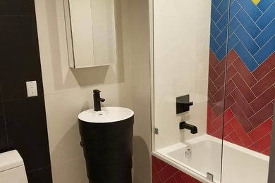 ニューヨークにあるお手頃価格の中くらいなコンテンポラリースタイルのおしゃれなマスターバスルーム (黒いキャビネット、ドロップイン型浴槽、シャワー付き浴槽	、一体型トイレ	、マルチカラーのタイル、セラミックタイル、マルチカラーの壁、セラミックタイルの床、ペデスタルシンク、白い床、引戸のシャワー) の写真