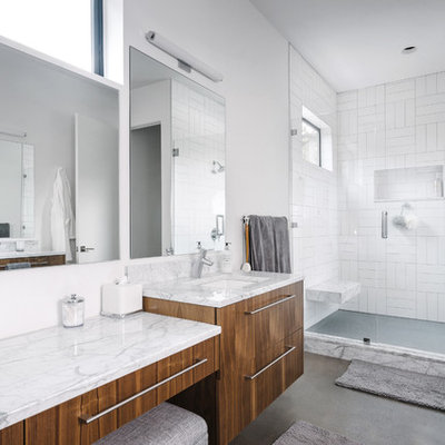 Inspiration for a mid-sized contemporary master white tile and stone tile concrete floor and gray floor bathroom remodel in Austin with flat-panel cabinets, a two-piece toilet, white walls, an undermount sink, a hinged shower door, medium tone wood cabinets, marble countertops and gray countertops