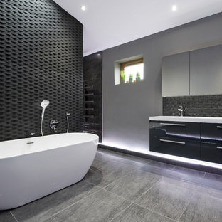 Photo of a large contemporary ensuite bathroom in West Midlands with black cabinets, a freestanding bath, black tiles, grey walls, porcelain flooring, white worktops, flat-panel cabinets and grey floors.