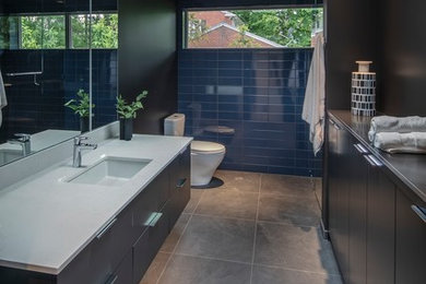 Inspiration for a mid-sized modern master blue tile ceramic tile and beige floor corner shower remodel in Grand Rapids with dark wood cabinets, a one-piece toilet, brown walls, an undermount sink, a hinged shower door and white countertops