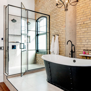 Modelo de cuarto de baño principal, industrial, con armarios con paneles lisos, puertas de armario con efecto envejecido, bañera exenta, ducha doble, sanitario de una pieza, baldosas y/o azulejos grises, baldosas y/o azulejos de cerámica, paredes blancas, suelo laminado, lavabo bajoencimera, encimera de cuarcita, suelo marrón, ducha con puerta con bisagras y encimeras blancas