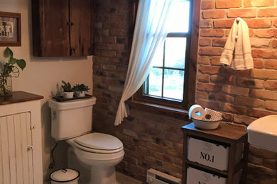 Cette image montre une salle de bain chalet de taille moyenne pour enfant avec une baignoire d'angle, un combiné douche/baignoire, WC séparés, un mur blanc, un lavabo de ferme, un sol multicolore, un plan de toilette blanc, meuble simple vasque et un mur en parement de brique.