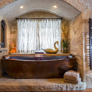 Immagine di una stanza da bagno padronale rustica con piastrelle in pietra e vasca freestanding