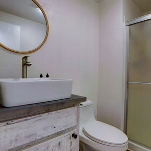 Imagen de cuarto de baño con ducha, rural, pequeño, con puertas de armario con efecto envejecido, encimeras grises, armarios con paneles lisos, ducha empotrada, sanitario de una pieza, paredes blancas, suelo laminado, lavabo sobreencimera, encimera de acrílico, suelo marrón y ducha con puerta corredera