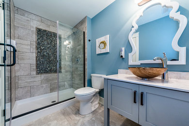 他の地域にある中くらいなビーチスタイルのおしゃれなバスルーム (浴槽なし) (シェーカースタイル扉のキャビネット、青いキャビネット、アルコーブ型シャワー、分離型トイレ、グレーのタイル、磁器タイル、青い壁、磁器タイルの床、ベッセル式洗面器、大理石の洗面台、グレーの床、開き戸のシャワー) の写真
