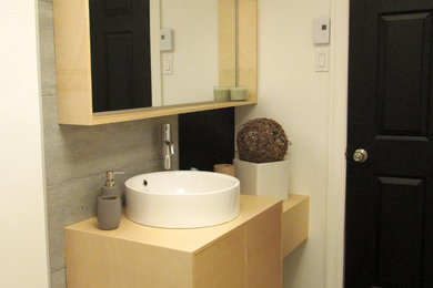 モントリオールにあるお手頃価格の小さな北欧スタイルのおしゃれな浴室 (フラットパネル扉のキャビネット、淡色木目調キャビネット、グレーのタイル、白い壁、クッションフロア、ベッセル式洗面器、木製洗面台) の写真