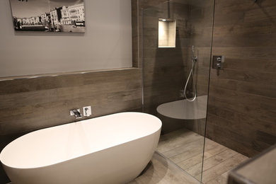 Idée de décoration pour une grande salle de bain minimaliste en bois brun avec un placard en trompe-l'oeil, une baignoire indépendante, un espace douche bain, WC suspendus, un carrelage gris, des carreaux de porcelaine, un mur gris, un sol en carrelage de porcelaine, une vasque, un plan de toilette en bois, un sol gris et aucune cabine.