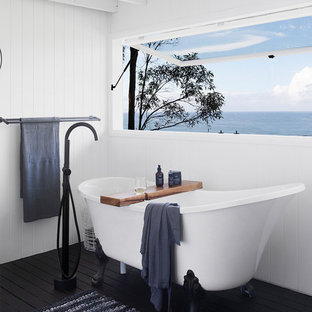 Beach style bathroom in Sunshine Coast with a claw-foot tub, white walls, painted wood floors and black floor.