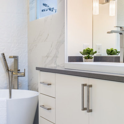 Inspiration for a mid-sized modern master white tile and porcelain tile porcelain tile and white floor bathroom remodel in Seattle with flat-panel cabinets, white cabinets, a one-piece toilet, white walls, a trough sink, quartz countertops, a hinged shower door and gray countertops