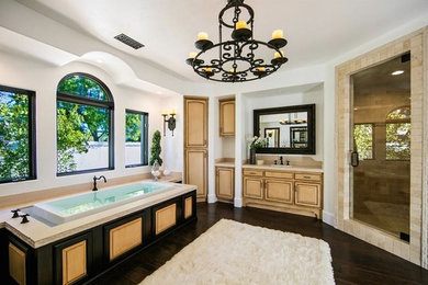 Inspiration for a large mediterranean master dark wood floor and brown floor drop-in bathtub remodel in Orange County with raised-panel cabinets, light wood cabinets, brown walls and an undermount sink