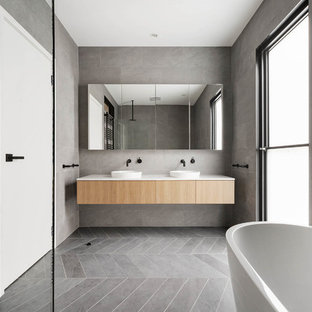 Inspiration for a contemporary bathroom in Melbourne with flat-panel cabinets, light wood cabinets, a freestanding tub, gray tile, grey walls, a vessel sink, grey floor and white benchtops.