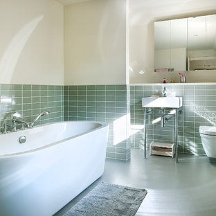 Photo of a mid-sized contemporary bathroom in Hampshire with a freestanding tub, a wall-mount toilet, ceramic tile, white walls, linoleum floors, green tile and a console sink.
