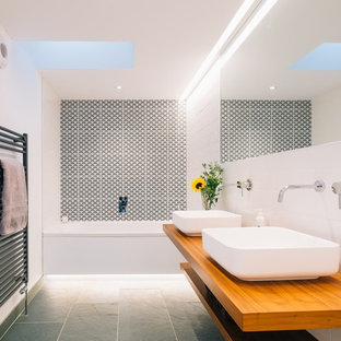 Photo of a mid-sized scandinavian bathroom in Cornwall with open cabinets, light wood cabinets, a drop-in tub, black and white tile, white tile, white walls, concrete floors, wood benchtops and brown benchtops.