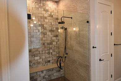Large trendy master brown tile and porcelain tile porcelain tile and multicolored floor bathroom photo in Raleigh with recessed-panel cabinets, medium tone wood cabinets, quartzite countertops, a one-piece toilet, brown walls, an undermount sink, a hinged shower door and beige countertops