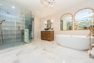 Photo of a large contemporary ensuite bathroom in Orange County with freestanding cabinets, dark wood cabinets, a freestanding bath, a corner shower, grey tiles, multi-coloured tiles, porcelain tiles, beige walls, ceramic flooring, a vessel sink, marble worktops, beige floors, a hinged door and white worktops.