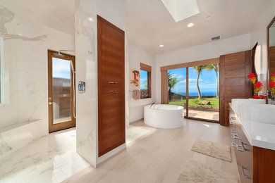 ハワイにある高級な広いトロピカルスタイルのおしゃれなマスターバスルーム (フラットパネル扉のキャビネット、濃色木目調キャビネット、置き型浴槽、オープン型シャワー、白い壁、白いタイル、石スラブタイル、淡色無垢フローリング、ベッセル式洗面器、クオーツストーンの洗面台、ベージュの床、オープンシャワー) の写真