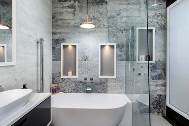 Exemple d'une petite salle de bain tendance avec des portes de placard noires, une baignoire indépendante, une douche ouverte, un plan de toilette en surface solide, WC suspendus, des carreaux de porcelaine, un mur gris, une vasque, un sol gris, aucune cabine, un plan de toilette blanc, une niche, meuble simple vasque, meuble-lavabo suspendu et un plafond voûté.