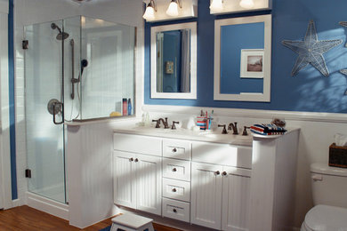 Inspiration for a mid-sized tropical master medium tone wood floor alcove shower remodel in Austin with an integrated sink, beaded inset cabinets, white cabinets, solid surface countertops, a two-piece toilet and blue walls