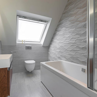 Photo of a medium sized contemporary bathroom in London with flat-panel cabinets, dark wood cabinets, a corner bath, a wall mounted toilet, grey walls, a wall-mounted sink, grey floors and grey tiles.