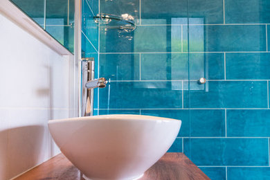 Cette photo montre une petite salle d'eau tendance avec un placard en trompe-l'oeil, des portes de placard blanches, une douche d'angle, WC à poser, des carreaux de céramique, un mur bleu, un sol en carrelage de porcelaine, un plan de toilette en bois et un carrelage bleu.