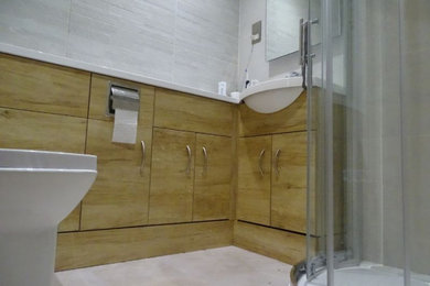 Inspiration for a small contemporary ensuite bathroom in Hampshire with flat-panel cabinets, light wood cabinets, a corner shower, a wall mounted toilet, grey tiles, ceramic tiles, a built-in sink, a sliding door, white worktops, a single sink and a built in vanity unit.