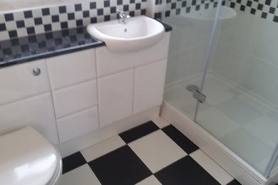 This is an example of a medium sized modern bathroom in Other with flat-panel cabinets, white cabinets, a built-in bath, a corner shower, a two-piece toilet, black and white tiles, ceramic tiles, white walls, ceramic flooring, a built-in sink, laminate worktops, multi-coloured floors, a hinged door and black worktops.