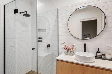 Photo of a medium sized contemporary ensuite bathroom in Melbourne with light wood cabinets, a corner shower, white tiles, ceramic tiles, white walls, ceramic flooring, a vessel sink, engineered stone worktops, brown floors, a hinged door and white worktops.