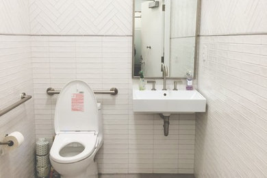 ニューヨークにあるモダンスタイルのおしゃれな浴室 (一体型トイレ	、白いタイル、白い壁、磁器タイルの床、壁付け型シンク) の写真
