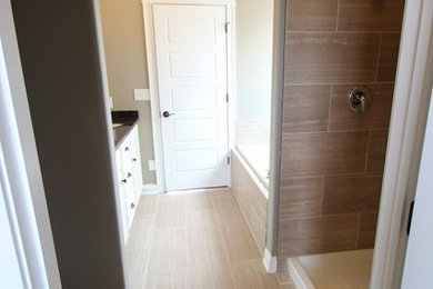 Inredning av ett en-suite badrum, med ett undermonterad handfat, luckor med upphöjd panel, vita skåp, granitbänkskiva, ett platsbyggt badkar, en hörndusch, beige kakel, grå väggar och klinkergolv i keramik
