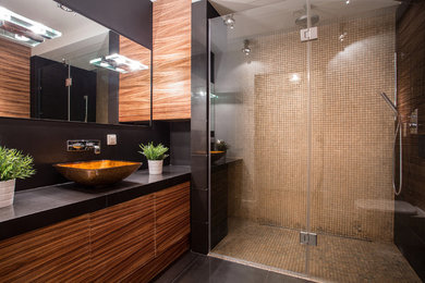 Example of a mid-sized minimalist 3/4 beige tile and glass tile porcelain tile walk-in shower design in Atlanta with flat-panel cabinets, medium tone wood cabinets, a wall-mount toilet, black walls, a vessel sink and quartz countertops