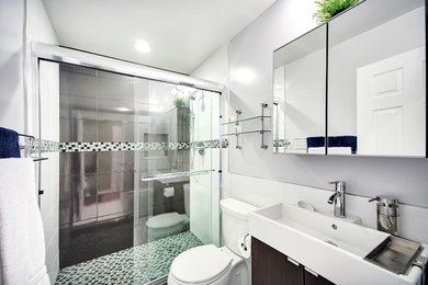 Modern inredning av ett badrum, med en dusch i en alkov, en toalettstol med separat cisternkåpa, grå kakel, porslinskakel, ett integrerad handfat, släta luckor och skåp i mörkt trä