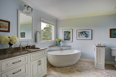 Example of a large danish master porcelain tile and beige floor freestanding bathtub design in Other with raised-panel cabinets, white cabinets, a one-piece toilet, blue walls, an undermount sink and granite countertops