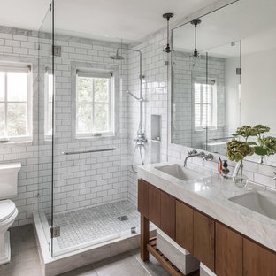 Ejemplo de cuarto de baño principal, de estilo de casa de campo, con armarios con paneles lisos, puertas de armario de madera en tonos medios, ducha esquinera, sanitario de dos piezas, baldosas y/o azulejos blancos, baldosas y/o azulejos de cemento, paredes blancas, lavabo bajoencimera, suelo gris, ducha con puerta con bisagras y encimeras blancas