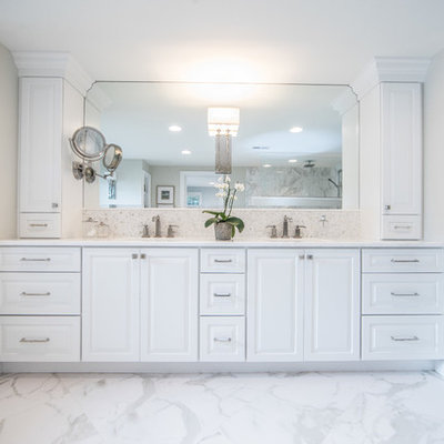 Example of a large mountain style master white tile and stone tile marble floor and multicolored floor drop-in bathtub design in DC Metro with raised-panel cabinets, white cabinets, gray walls, an undermount sink, marble countertops, a two-piece toilet and white countertops