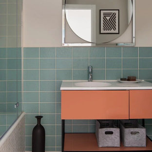Idéer för att renovera ett mellanstort funkis vit vitt en-suite badrum, med släta luckor, orange skåp, ett undermonterat badkar, en dusch/badkar-kombination, en vägghängd toalettstol, blå kakel, keramikplattor, beige väggar, cementgolv, ett konsol handfat, bänkskiva i akrylsten, orange golv och dusch med duschdraperi