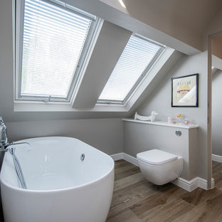 Photo of a small contemporary bathroom in Surrey with a freestanding bath, a wall mounted toilet, grey walls, dark hardwood flooring, a wall-mounted sink and brown floors.