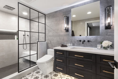 Mid-sized urban beige tile and porcelain tile porcelain tile and multicolored floor sauna photo in Other with shaker cabinets, black cabinets, a one-piece toilet, gray walls, an undermount sink, quartz countertops, a hinged shower door and beige countertops