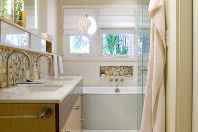 Foto på ett mellanstort funkis en-suite badrum, med ett undermonterad handfat, släta luckor, skåp i ljust trä, marmorbänkskiva, ett fristående badkar, en hörndusch, flerfärgad kakel, glaskakel, beige väggar och kalkstensgolv