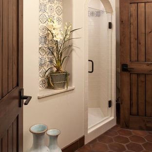 Photo of a large mediterranean 3/4 bathroom in Santa Barbara with an undermount sink, recessed-panel cabinets, dark wood cabinets, an alcove shower, a two-piece toilet, beige tile, terra-cotta tile, white walls and terra-cotta floors.