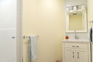 Ejemplo de cuarto de baño contemporáneo de tamaño medio con armarios con paneles lisos, puertas de armario blancas, sanitario de una pieza, baldosas y/o azulejos blancos, baldosas y/o azulejos de cemento, paredes amarillas, suelo de baldosas de cerámica, lavabo bajoencimera y encimera de granito