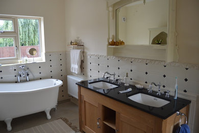 Photo of a classic family bathroom in Other with freestanding cabinets, light wood cabinets, a freestanding bath, a two-piece toilet, an integrated sink and solid surface worktops.