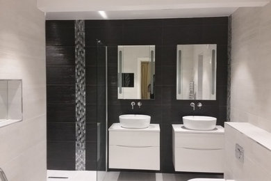 Photo of a large contemporary bathroom in Hertfordshire with flat-panel cabinets, white cabinets, a freestanding bath, a walk-in shower, black tiles, mosaic tiles and porcelain flooring.