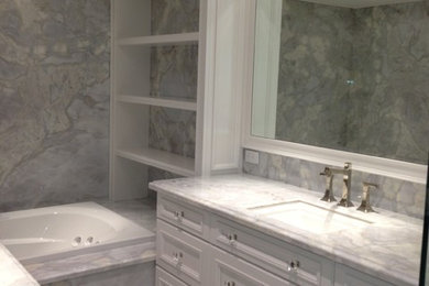 Large transitional master marble tile drop-in bathtub photo in Montreal with recessed-panel cabinets, white cabinets, an undermount sink and marble countertops