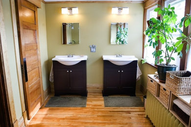 Modelo de cuarto de baño de tamaño medio con lavabo integrado, armarios estilo shaker, puertas de armario de madera en tonos medios, paredes verdes, suelo de madera clara y aseo y ducha
