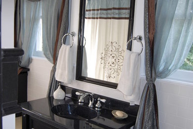 Modelo de cuarto de baño retro con lavabo integrado, armarios tipo mueble, puertas de armario de madera en tonos medios, encimera de cuarzo compacto, bañera empotrada, sanitario de dos piezas, baldosas y/o azulejos negros y baldosas y/o azulejos de cerámica