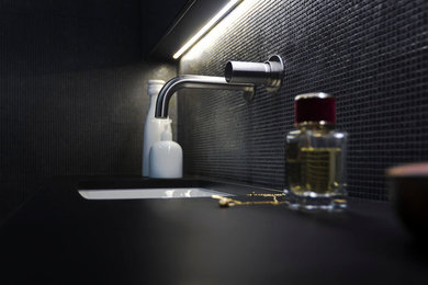 Small contemporary shower room bathroom in London with glass-front cabinets, black cabinets, a submerged bath, a shower/bath combination, a wall mounted toilet, black tiles, mosaic tiles, black walls, mosaic tile flooring, a submerged sink and marble worktops.
