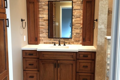 Inspiration for a mid-sized transitional master corner shower remodel in Houston with recessed-panel cabinets, medium tone wood cabinets, a two-piece toilet, beige walls, an undermount sink, solid surface countertops and a hinged shower door